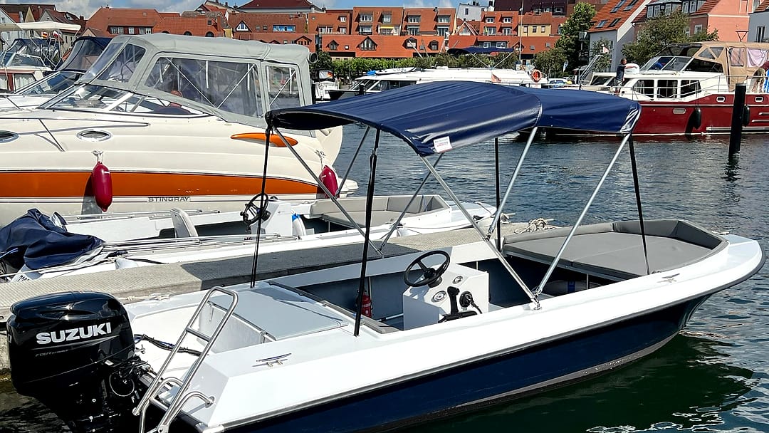 Motorboot mit 50-PS-Suzuki-Außenborder, blauem Bimini-Sonnendach und Mittelkonsole am Steg im Stadthafen Waren an der Müritz.