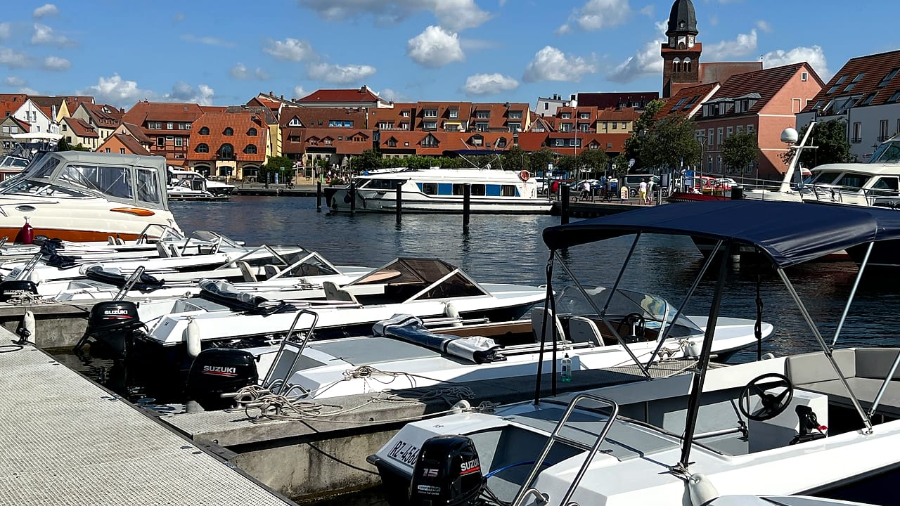 Blick über den Stadthafen Waren an der Müritz mit kleinen Motorbooten am Steg und der Marienkirche im Hintergrund.