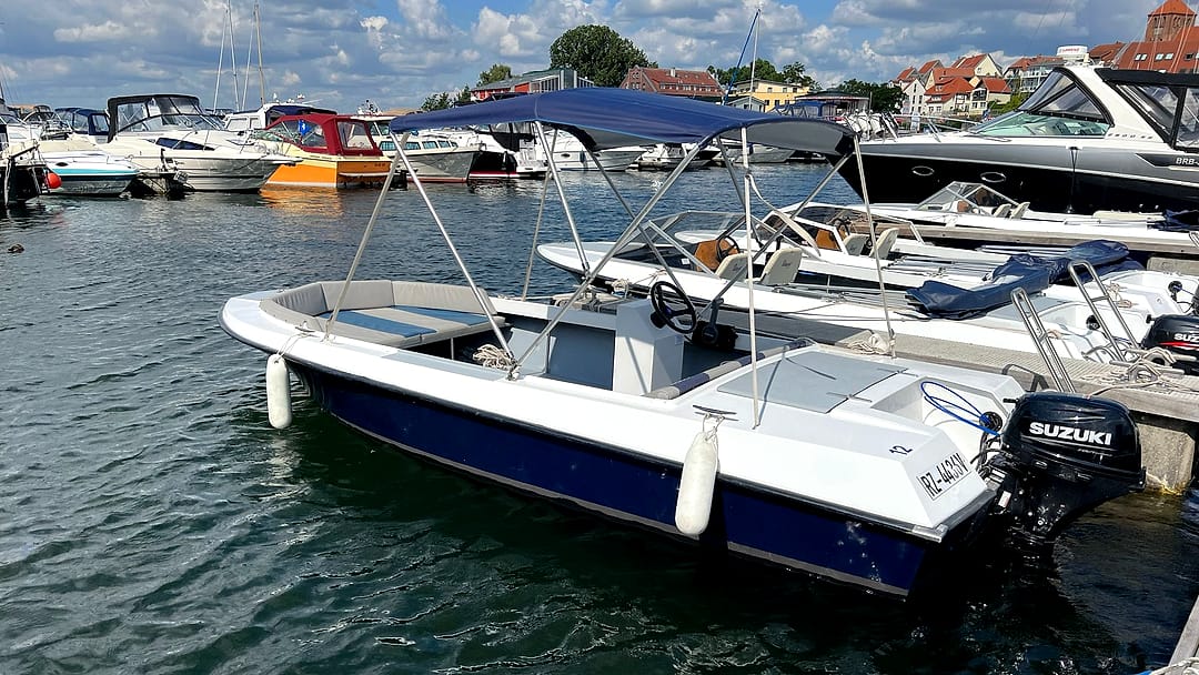 Führerscheinfreies Konsolenboot (Typ 3) mit blauem Bimini-Sonnendach und Suzuki-Außenborder vor der Kulisse von Waren an der Müritz.
