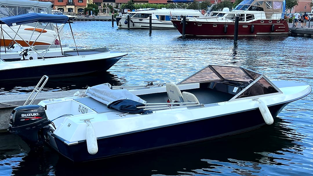 Führerscheinfreies Motorboot (Typ 4) in Dunkelblau-Weiß mit Holz-Windschutz und Suzuki-Außenborder am Steg im Stadthafen Waren.